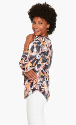 Load image into Gallery viewer, Left side top half view of a woman wearing the nic and zoe zenergized live in top. This top has a large grey, pink, and mustard floral print. The top also has long sleeves and a v-neck.
