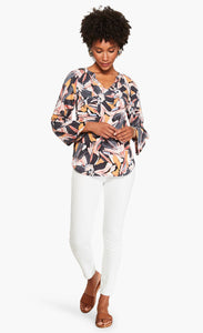Front full body view of a woman wearing the nic and zoe zenergized live in top. This top has a large grey, pink, and mustard floral print. The top also has long sleeves and a v-neck.