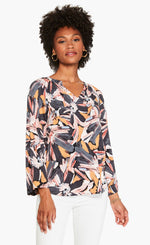 Load image into Gallery viewer, Front top half view of a woman wearing the nic and zoe zenergized live in top. This top has a large grey, pink, and mustard floral print. The top also has long sleeves and a v-neck.
