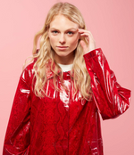 Load image into Gallery viewer, Front top half view of a woman with blonde hair wearing the red Courtney Raincoat from Nikki Jones. This raincoat has long sleeves, a hood, and snakeskin print.
