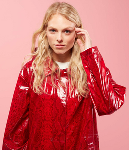 Front top half view of a woman with blonde hair wearing the red Courtney Raincoat from Nikki Jones. This raincoat has long sleeves, a hood, and snakeskin print.