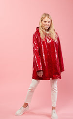 Load image into Gallery viewer, Front full body view of a woman with blonde hair wearing white pants, white shoes, and the red Courtney Raincoat from Nikki Jones. This raincoat has long sleeves, a hood, snakeskin print, and comes down below the hips
