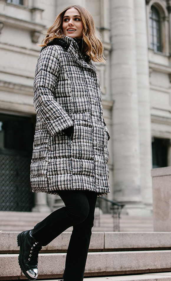 Right side action shot of a model walking around town wearing black pants and the nikki jones plaid jeannie coat. This coat is white with black and beige/grey plaid print.