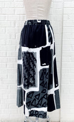 Load image into Gallery viewer, Back view of the crea concept black and white print pant. This pant has an abstract print on it, a wide leg, and an off-center back that makes it appear as a skirt.
