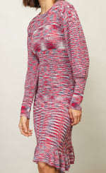 Load image into Gallery viewer, Left sided front full body view of a woman wwearing the Line + Dot Noa Sweater Dress. This dress has a mixed pink and blue knit fabric, a fitted silhouette with a ruffled hem that sits at the knees and large sleeves with fitted cuffs.
