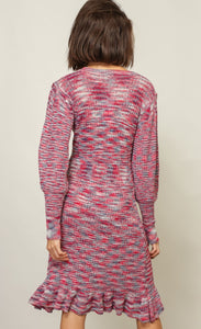Back full body view of a woman with wearing the Line + Dot Noa Sweater Dress. This dress has a mixed pink and blue knit fabric, a fitted silhouette with a ruffled hem that sits at the knees and large sleeves with fitted cuffs.
