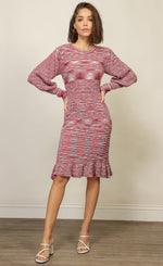 Load image into Gallery viewer, Front full body view of a woman with her hands on her hip and wearing the Line + Dot Noa Sweater Dress. This dress has a mixed pink and blue knit fabric, a fitted silhouette with a ruffled hem that sits at the knees and large sleeves with fitted cuffs.
