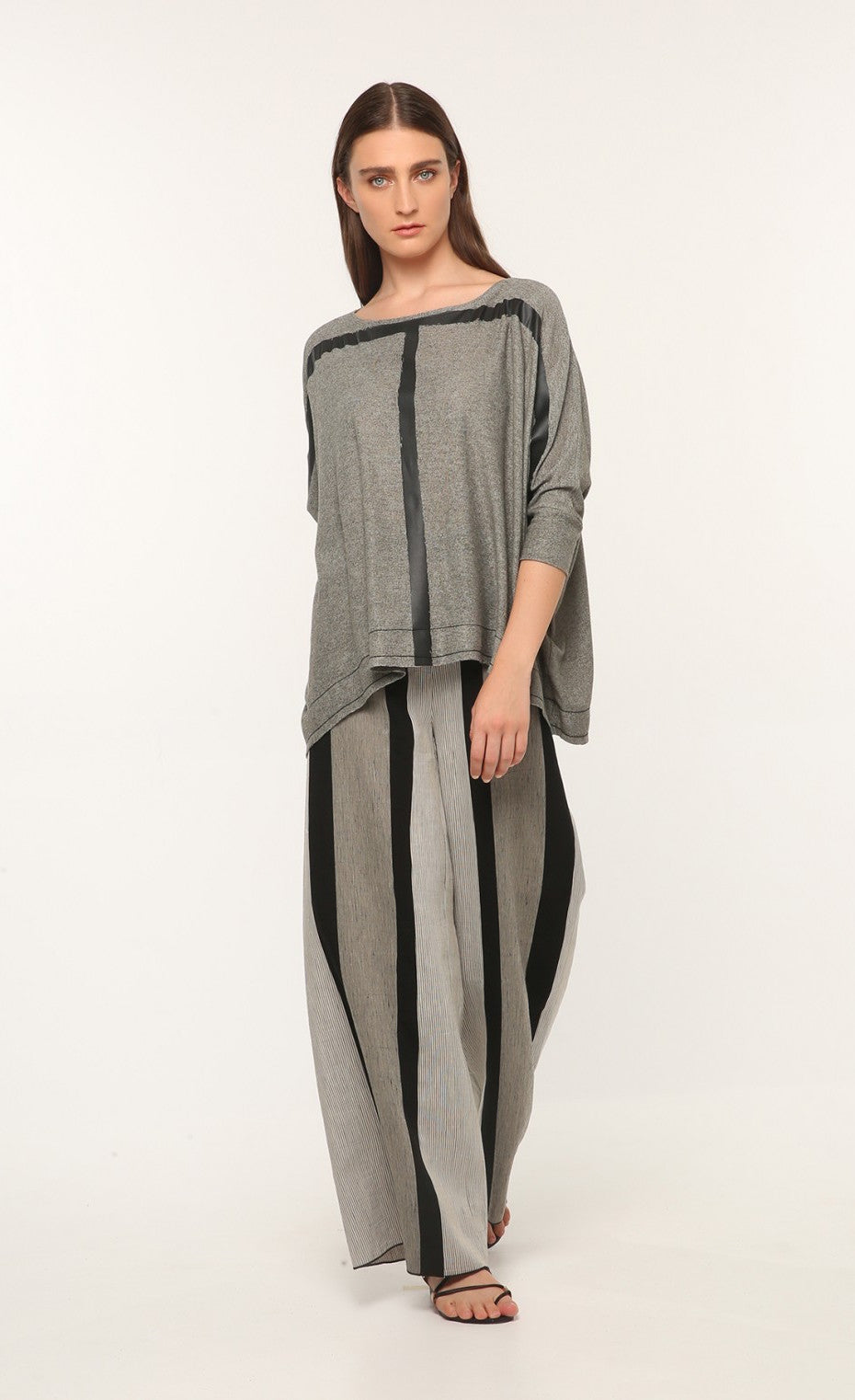 Front full body view of a woman wearing the ozai n ku marjoram top. This top is dark grey with two black painted lines on it that form a t shape. The top has 3/4 length sleeves.