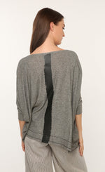 Load image into Gallery viewer, Back top half view of a woman wearing the ozai n ku marjoram top. This top is dark grey with a black painted line down the middle of the back. The top has 3/4 length sleeves.
