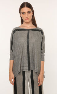 Front top half view of a woman wearing the ozai n ku marjoram top. This top is dark grey with two black painted lines on it that form a t shape. The top has 3/4 length sleeves.