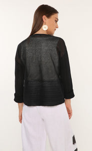 Back top half view of a woman wearing the ozai n ku mimosa knit top. This top is black and translucent. It has a darker pattern running across the bottom of the back and on the long sleeves. 