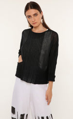 Load image into Gallery viewer, Front top half view of a woman wearing the ozai n ku mimosa knit top. This top is black and translucent. It has a darker pattern running down the middle of the front, long sleeves, and on the two front pockets. 
