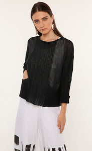 Front top half view of a woman wearing the ozai n ku mimosa knit top. This top is black and translucent. It has a darker pattern running down the middle of the front, long sleeves, and on the two front pockets. 