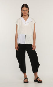 Front full body view of a woman wearing the ozai n ku tuberose top. This top is white and off-white. The front has cap sleeves, black little sketched designs, a split v-neck, and a drawstring waist on the right side.