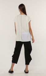 Load image into Gallery viewer, Back full body view of a woman wearing the ozai n ku tuberose top. This top is white and off-white. It has cap sleeves and a contrasting black stitch down the middle.
