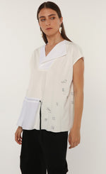 Load image into Gallery viewer, Front top half view of a woman wearing the ozai n ku tuberose top. This top is white and off-white. The front has cap sleeves, black little sketched designs, a split v-neck, and a drawstring waist on the right side.

