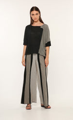 Load image into Gallery viewer, Front full body view of a woman wearing the ozai n ku vervain top. This top is black on the front right side and dark grey on the front left side. The sleeves are elbow length and the two tones come together to create a fold over effect near the neck. The front also has a front pocket on the left side.
