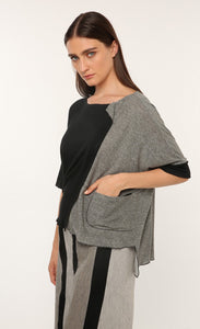 Front top half view of a woman wearing the ozai n ku vervain top. This top is black on the front right side and dark grey on the front left side. The sleeves are elbow length and the two tones come together to create a fold over effect near the neck. The front also has a front pocket on the left side.