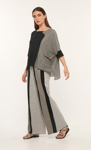 Front full body view of a woman wearing the ozai n ku vervain top. This top is black on the front right side and dark grey on the front left side. The sleeves are elbow length and the two tones come together to create a fold over effect near the neck. The front also has a front pocket on the left side.