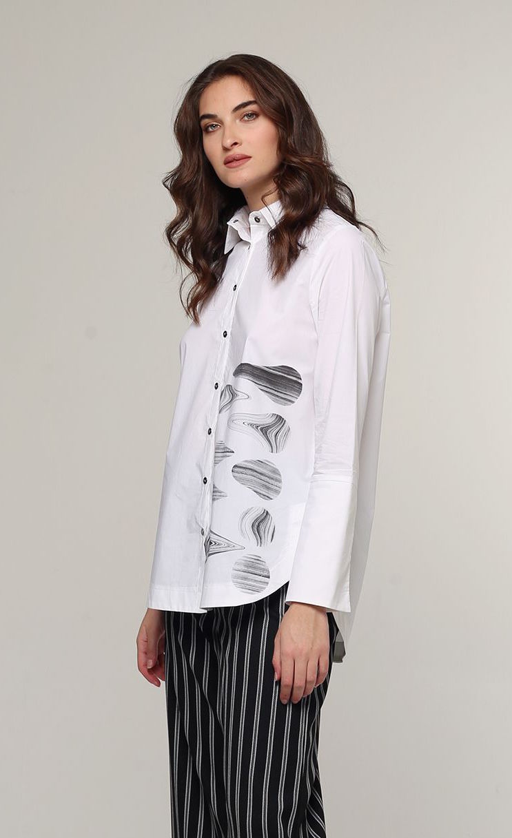 Front top half view of a woman wearing the Ozai N Ku White Shirt. This shirt is a classic white shirt with a grey marble abstract print on the front left side of the shirt. The shirt has a button down front and long sleeves.
