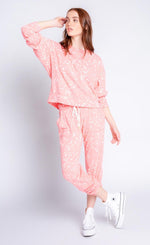 Load image into Gallery viewer, Front full body view of a woman wearing the pj salvage flick of a brush set. This set is coral with white paint drops. The top has long banded sleeves and the bottoms are joggers with a white drawstring.
