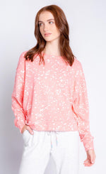 Load image into Gallery viewer, Front top half view of a woman wearing the pj salvage flick of a brush long sleeve top. This top is coral with white paint drops.
