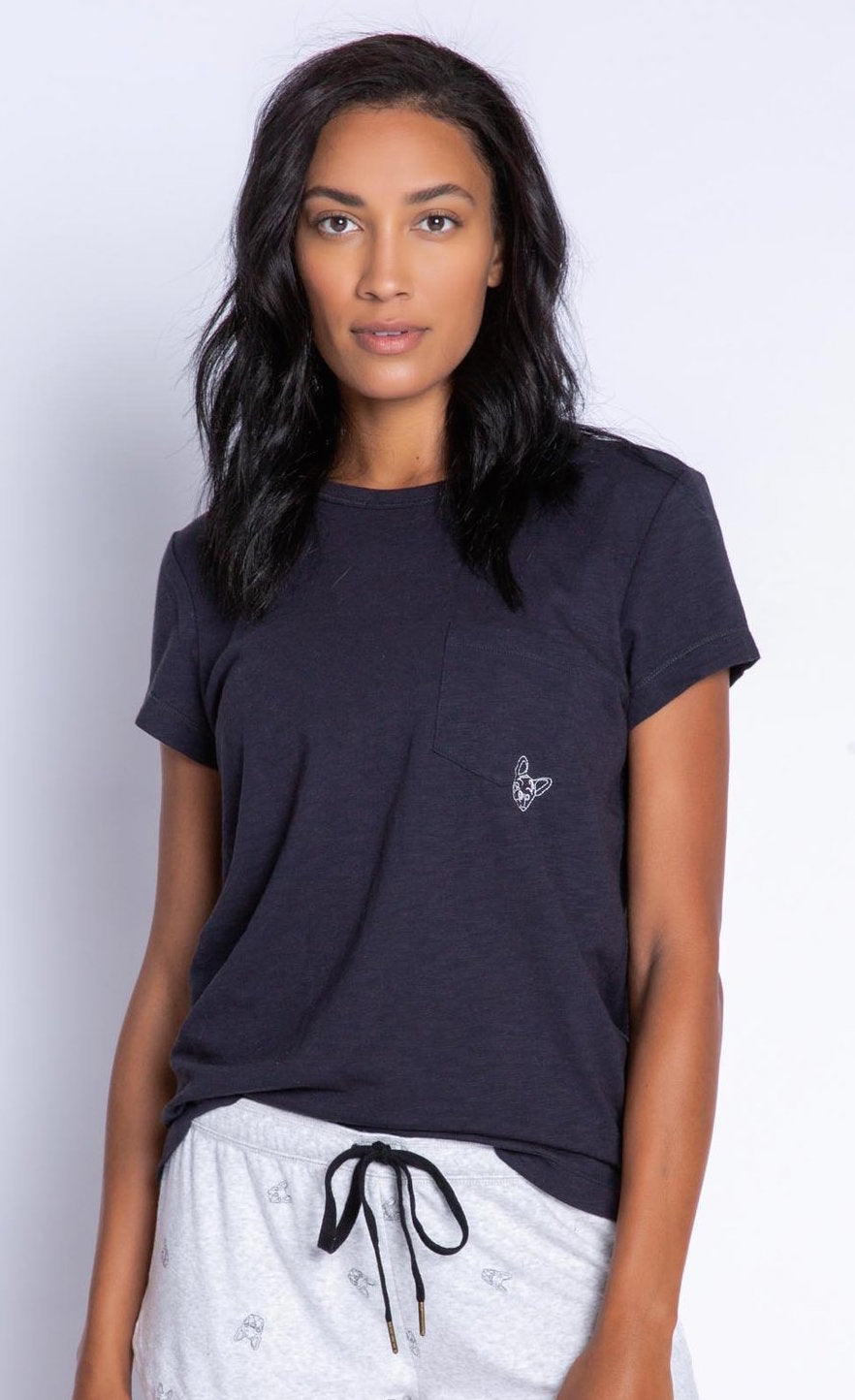 Front top half view of a woman wearing the PJ Salvage Lily Rose Tee. The short sleeve t-shirt is black and has a single front pocket on the left side with a tiny french bulldog face printed on it.
