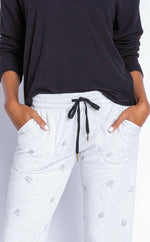 Load image into Gallery viewer, Close up view of a woman wearing the Lily Rose Banded Pant. The pant is a heathered light grey and has a black tie waistband and black tiny french bulldog faces printed all over it.
