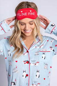 Front top half view of woman wearing the pj salvage love is a four legged word pj set. This set is light blue colored with cats printed all over it and red trim. The set has a button down shirt with long sleeves and a red sleep mask that says feline fine.