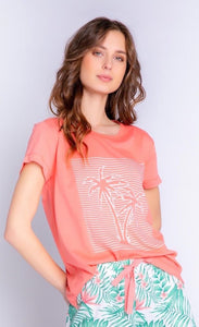 Front top half view of a woman wearing the pj salvage playful prints short sleeve tee and the pj salvage playful prints pant. This top is coral with white outlines of palm trees and stripes on the front. The bottoms are white with green palm leaves and coral detailing/a coral drawstring.