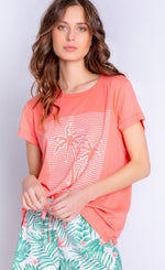 Load image into Gallery viewer, Front top half view of a woman wearing the pj salvage playful prints short sleeve tee and the pj salvage playful prints pant. This top is coral with white outlines of palm trees and stripes on the front. The bottoms are white with green palm leaves and coral detailing/a coral drawstring.
