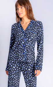 Front top half view of a woman wearing the pj salvage spot the dot pj set. This set is a long sleeve shirt and long pant. It is black with white dots lined in blue.