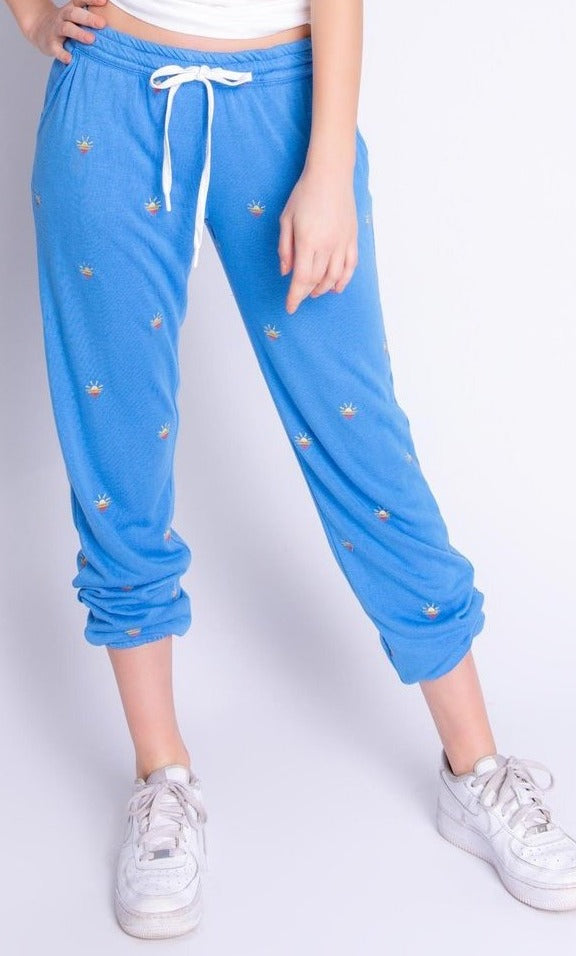 Front bottom half view of a woman wearing the pj salvage sun out banded pant. The pant is sky blue with tiny embroidered sunsets all over it.
