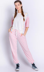 Load image into Gallery viewer, Front full body view of a woman wearing the PJ Salvage Sunset Hues short sleeve top and the pj salvage sunset hues banded pant. The top is white with yellow, blue, and pink tie dye on the sides. The bottoms are pink with crochet detailing on the sides and a banded hem. 

