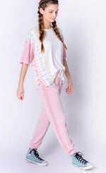 Load image into Gallery viewer, Front right side full body view of a woman wearing the PJ Salvage Sunset Hues short sleeve top and the pj salvage sunset hues banded pant. The top is white with yellow, blue, and pink tie dye on the sides. The bottoms are pink with crochet detailing on the sides and a banded hem. 
