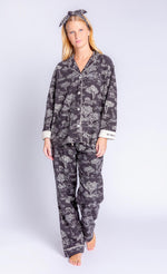 Load image into Gallery viewer, Front full body view of a woman wearing the PJ Salvage Go Wild PJ Set. This set is black with a white safari print all over it. It includes a long sleeve shirt and long pants. The cuffs are white and say go wild. The woman is also wearing a matching headband with a top knot.
