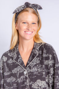Front top half view of a woman wearing the PJ Salvage Go Wild PJ Set. This set is black with a white safari print all over it. The woman is also wearing a matching headband with a top knot.