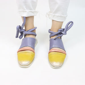 Front view of a pair of the papucei etsy shoe. This shoe is flat. The front leather portion that covers the toe is yellow. The strap over the inset is pink and the rest of the shoe leather is purple. This shoe also has purple leather ankle ties.