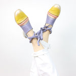 Load image into Gallery viewer, front view of a woman wearing a pair of the papucei etsy shoe. This shoe is flat. The front leather portion that covers the toe is yellow. The strap over the inset is pink and the rest of the shoe leather is purple. This shoe also has purple leather ankle ties.
