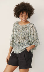 Load image into Gallery viewer, Front top half view of a woman wearing black shorts and the part two ingeborg floral top. This top has a small blue/green floral print, a gathered round neck, and 3/4 length wide sleeves.
