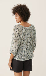 Load image into Gallery viewer, Back top half view of a woman wearing black shorts and the part two ingeborg floral top. This top has a small blue/green floral print, a gathered round neck, and 3/4 length wide sleeves.
