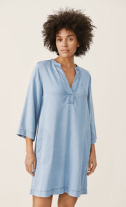 Front full body view of a woman wearing the part two ingeline dress. This dress is a light blue denim. It ends at the knees, has 3/4 length sleeves, and a v-neck. 