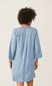 Back full body view of a woman wearing the part two ingeline dress. This dress is a light blue denim. It ends at the knees and has 3/4 length sleeves.