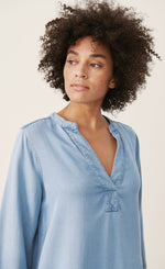 Load image into Gallery viewer, Front top half view of a woman wearing the part two ingeline dress. This dress is a light blue denim. It has 3/4 length sleeves and a v-neck. 
