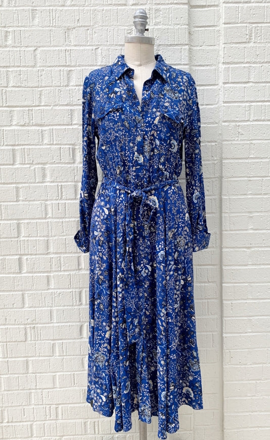 front full body view of a mannequin wearing the part two true paisley flower dress. This dress is ultramarine/vibrant blue color with white paisley floral print. The dress sits below the knees and has a button down front and tie belt.
