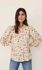 Load image into Gallery viewer, Front Top half view of a woman with her hands on her hips wearing the Part Two Hien Long Sleeved Paint shirt. This shirt is creme/light pink colored with multi-colored paint splattered dots all over it. The sleeves are puffer sleeves and the shirt has a button down front.
