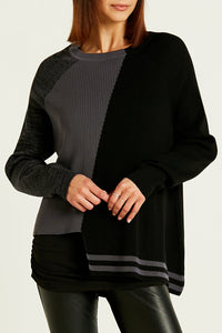 front top half view of a woman wearing black leather pants and the planet pima cotton 2 tone crewneck sweater. This sweater is black on the left side and grey on the right side. the left side also has a longer hem with grey striping, while the right side has a shorter hem with a washed black sleeve.