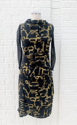 Load image into Gallery viewer, Front view of the porto popstar dress layered over a black mesh tee. This sleeveless dress is black with dijon newspaper letter print. The dress has a fitted silhouette with a draped mock neck.
