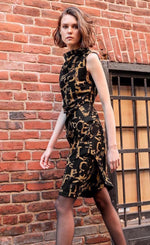 Load image into Gallery viewer, Front left side full body view of a woman wearing the porto popstar dress. This sleeveless dress is black with dijon newspaper letter print. The dress has a fitted silhouette with a draped mock neck.
