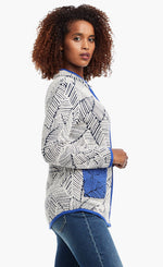 Load image into Gallery viewer, Side view of a woman wearing the Nic+Zoe New Leaf Jacket zipped close. The zip up jacket has a black and white leaf pattern and blue trim with two front blue patch pockets.
